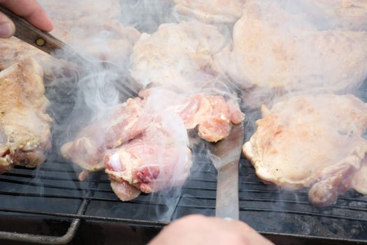 Turning over raw pork chops on grill. Smoke rising from heated grill