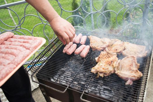 Grilling cevapi and pork chops. Putting raw meat on grill