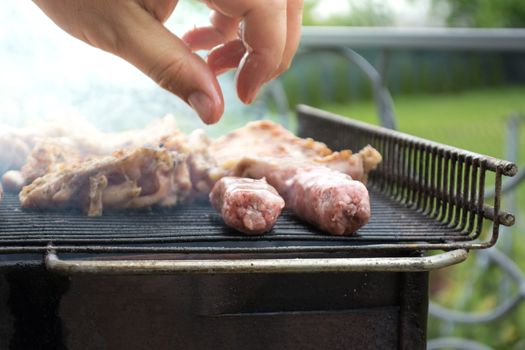 Grilling cevapi and pork chops. Putting raw meat on grill