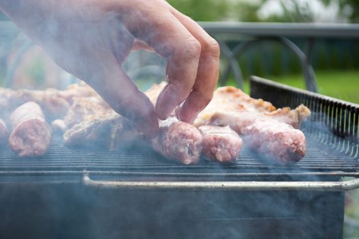 Grilling cevapi and pork chops. Putting raw meat on grill