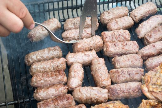 Grilling cevapi and pork chops. Hand visible in the shot