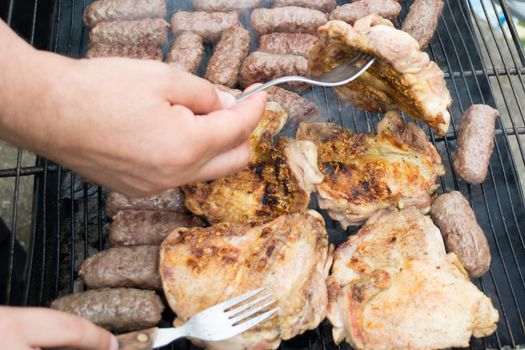 Grilling cevapi and pork chops. Hand visible in the shot