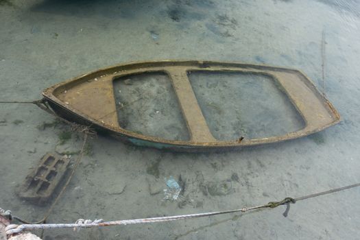 Small sunken boat in harbor submerged in shallow water and moored