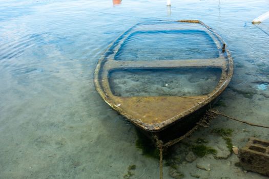 Small sunken boat in harbor submerged in shallow water and moored