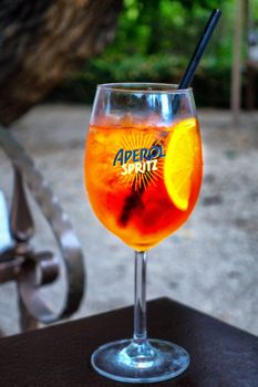 Aperol Spritz Popular Refreshing Summer Drink in Glas on table with orange slice and straw, close up,