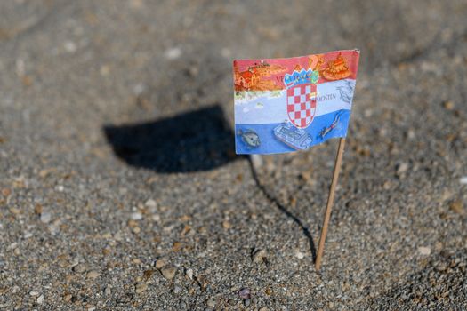 Touristic flag of Croatia picked in Sand on Beach, various travel destinations and map of Croatia printed on flag, cocktail flag