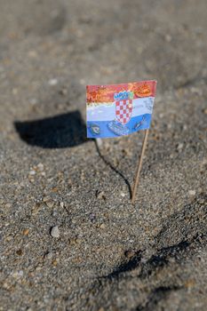 Touristic flag of Croatia picked in Sand on Beach, various travel destinations and map of Croatia printed on flag, cocktail flag