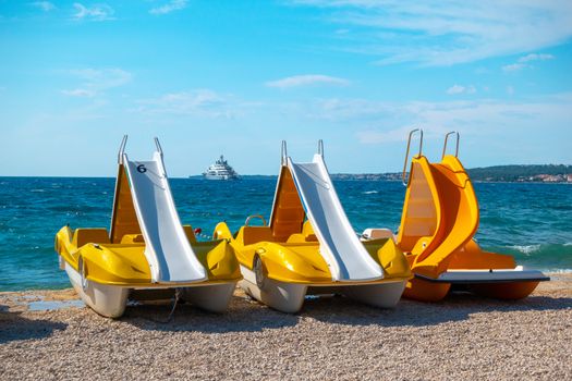 Colorful pedal boats, pedolinos on beach, yellow color, boat with slide, sea in the background