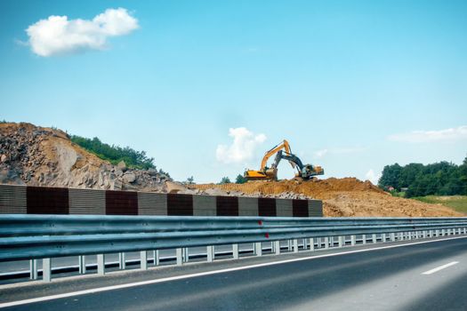 Two heavy, yellow and black excavators on construction site moving soil and rock, highway, road construction, booms are crossed
