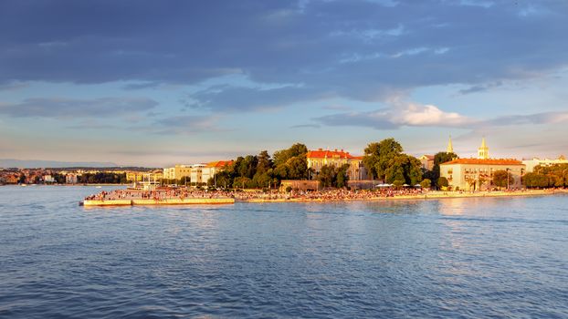 Ancient city of Zadar, Croatia as seen from the sea, waterfront with famous sea organ, cathedral in background, people gathering to watch the sunset
