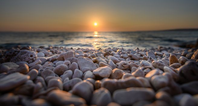 Beach pebbles at sunset, close up macro of stones in foreground, sea and setting sun in the back, centered