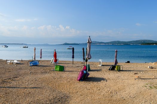 Beach in Turanj, small village in Dalmatia, Croatia, island of Pasman in background, sunchairs, parasols, umbrellas and beach requisites