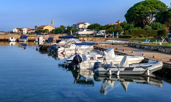 Turanj village harbor and waterfront view, Dalmatia, Croatia, small motor boats and sailing boats moored in harbor, sky reflecting in water, early morning
