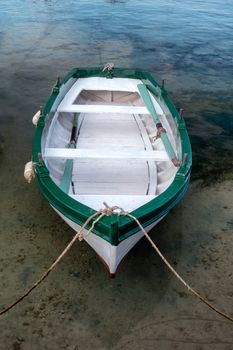 Small traditional wooden fishing boat in harbor, moored to the pier, sky reflecting in water, small water vessel