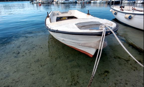 Small traditional wooden fishing boat in harbor, moored to the pier, sky reflecting in water, small water vessel