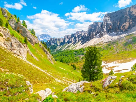Landscape of Dolomites with green meadows, blue sky, white clouds and rocky mountains.