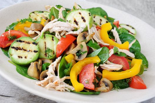 Warm chicken salad with spinach, tomato slices, sweet pepper, grilled zucchini, and champignons, all dressed with herbs and fragrant oil.