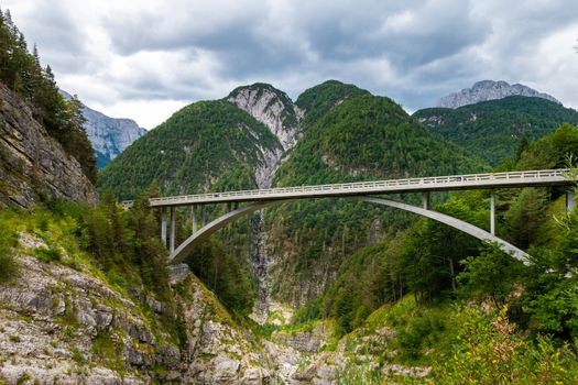 Arched bridge over a mountain river gorge in European Alps with mountain in background and cloudy skies. Mangart saddle pass in Julian alps, Slovenia