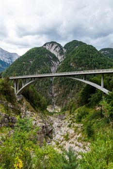 Mountain road with bridge spanning over a gorge in European Alps with mountain in background and cloudy skies near Mangart saddle pass in Julian alps, Slovenia
