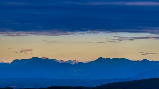 Dolomites in the morning with clouds above, sun rays illuminate the farthest mountain peaks, long distance panoramic shot