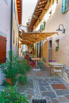 Small caffee, restaurant in narrow street in a medieval town with colorful tables and chairs, nobody, empty, umbrellas for shade