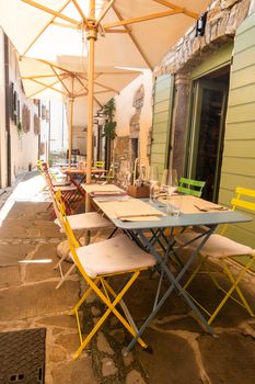 Small caffee, restaurant in narrow street in a medieval town with colorful tables and chairs, nobody, empty, umbrellas for shade