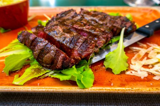 Traditional Italian Tagliata Steak with Parmesan and Salad as close-up on a plate with a steak knife