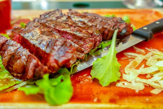 Top view of Traditional Italian Tagliata Steak with Parmesan and Green Salad, sparkled with Balsamico vinegar as close-up on a plate