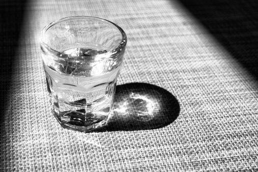 Black and white small glass of liquor, grappa glass, traditional Italian drink, sparkles in glass, framed with shadow