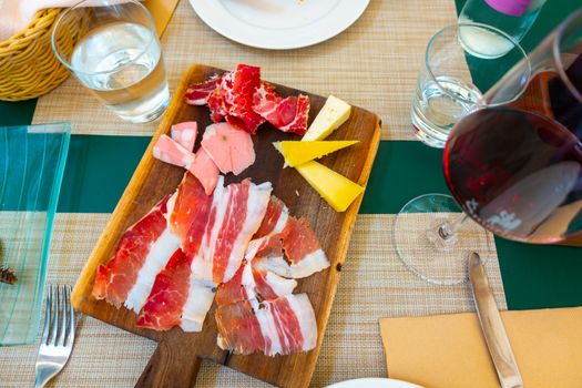 Italian style cold meat plate with cheese on wooden board with pancetta, Prosciutto, cheese and mortadella on table with glass of red wine
