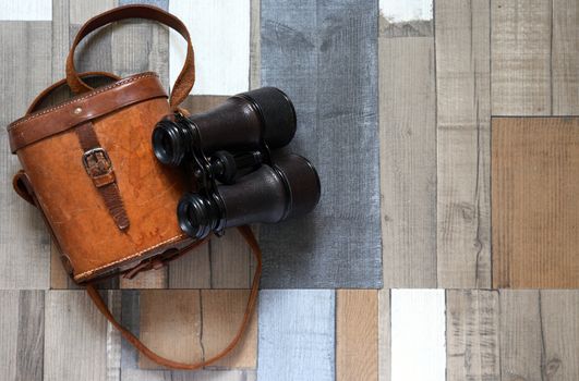 Old binoculars with leather case on color wooden background