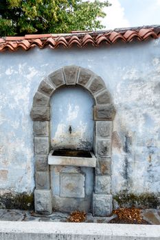 Vintage drinking water fountain in Smartno, Goriska Brda, Slovenia, niche in brick wall, stone arch above water tap