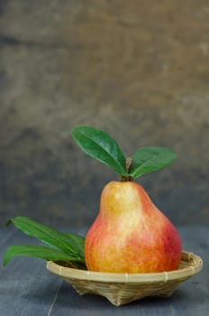 Ripe red pears with green leaves on basket over wooden table