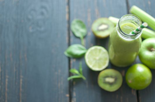 Green smoothie bottle with ingredients on wooden table