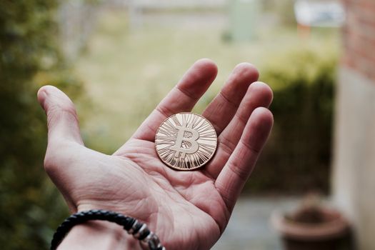 Digital currency physical gold bitcoin coin on man hand with bracelet.