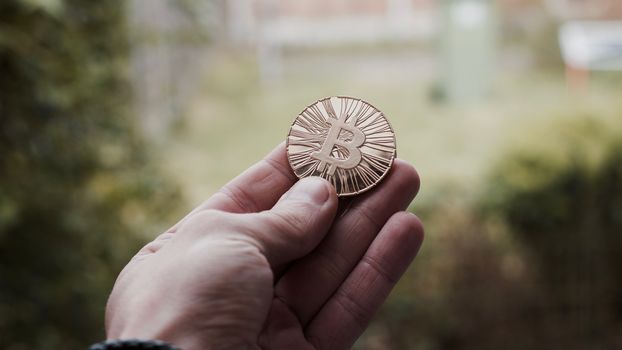 Digital currency physical gold bitcoin coin in man hand with black bracelet.