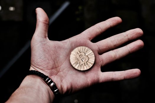 Digital currency physical gold bitcoin coin in man hand with black bracelet.