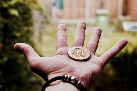 Digital currency physical gold bitcoin coin in man hand with black bracelet.