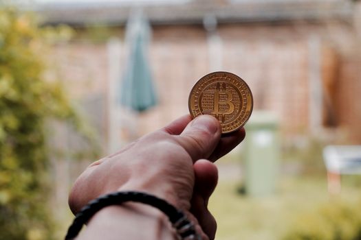 Digital currency physical gold bitcoin coin in man hand with black bracelet.