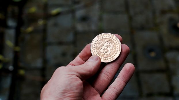 Digital currency physical gold bitcoin coin in man hand with black bracelet.
