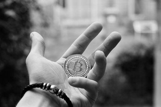 Digital currency physical gold bitcoin coin in man hand with black bracelet.