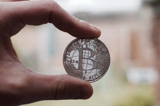 Cryptocurrency physical silver bitcoin coin holding in man fingers.