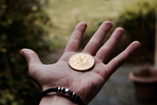 Digital currency physical gold litecoin coin on man hand with black bracelet.