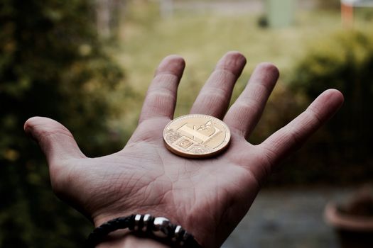 Digital currency physical gold litecoin coin on man hand with black bracelet.