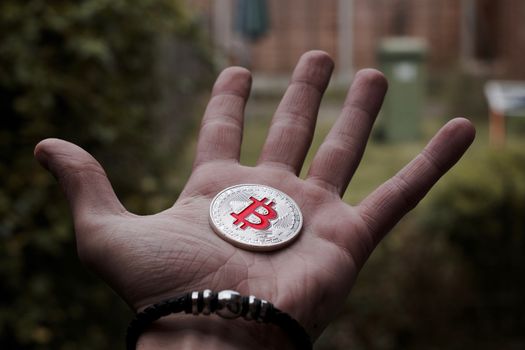 Cryptocurrency physical silver bitcoin coin on man hand with black bracelet outdoor.