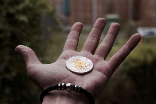 Cryptocurrency physical silver bitcoin coin on man hand with black bracelet outdoor.