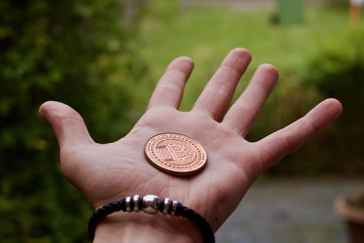 Digital currency physical brass bitcoin coin in man hand with black bracelet.