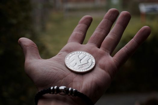 Digital currency physical silver litecoin coin on man hand with black bracelet. Outdoor.