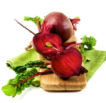 One Full Body Fresh Raw Organic Beet Two Halves with Green Beet Tops on Wooden Board and Napkin isolated on White background