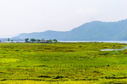 Photograph of winter season: A colourful lake, mountain, clear sky and farm land. Wide angle landscape of Pokhara Lake at Kathmandu Nepal. Vintage film look. Vacation Freedom, Simplicity Concept.